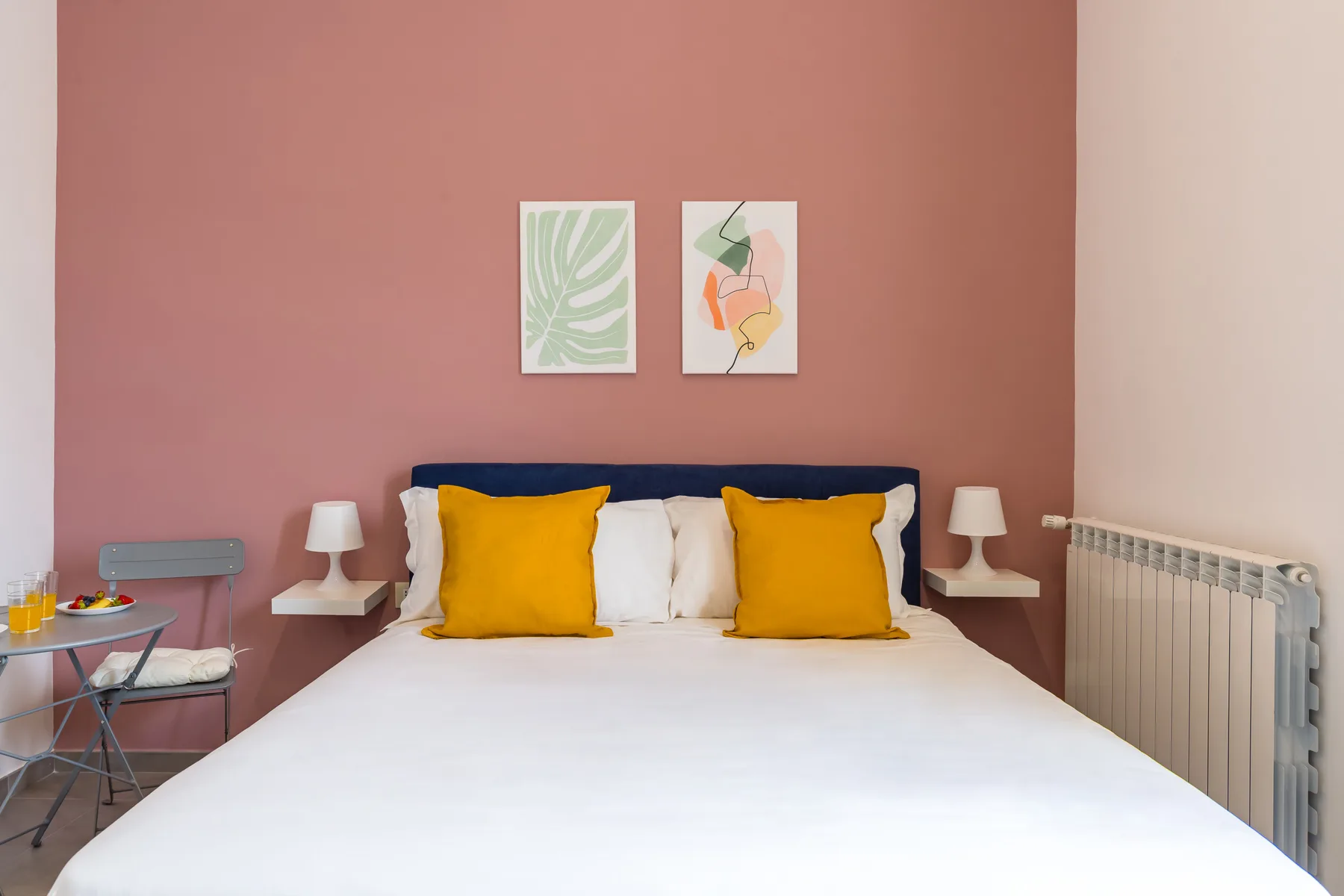 Un dormitorio con una cama bien tendida, almohadas amarillas y cuadros en la pared.