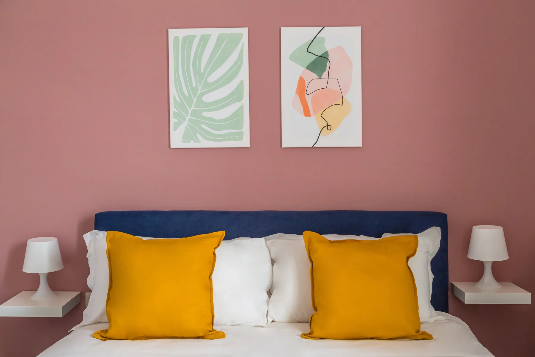 Un dormitorio con una cama, almohadas de colores vivos y dos cuadros sobre el cabecero.