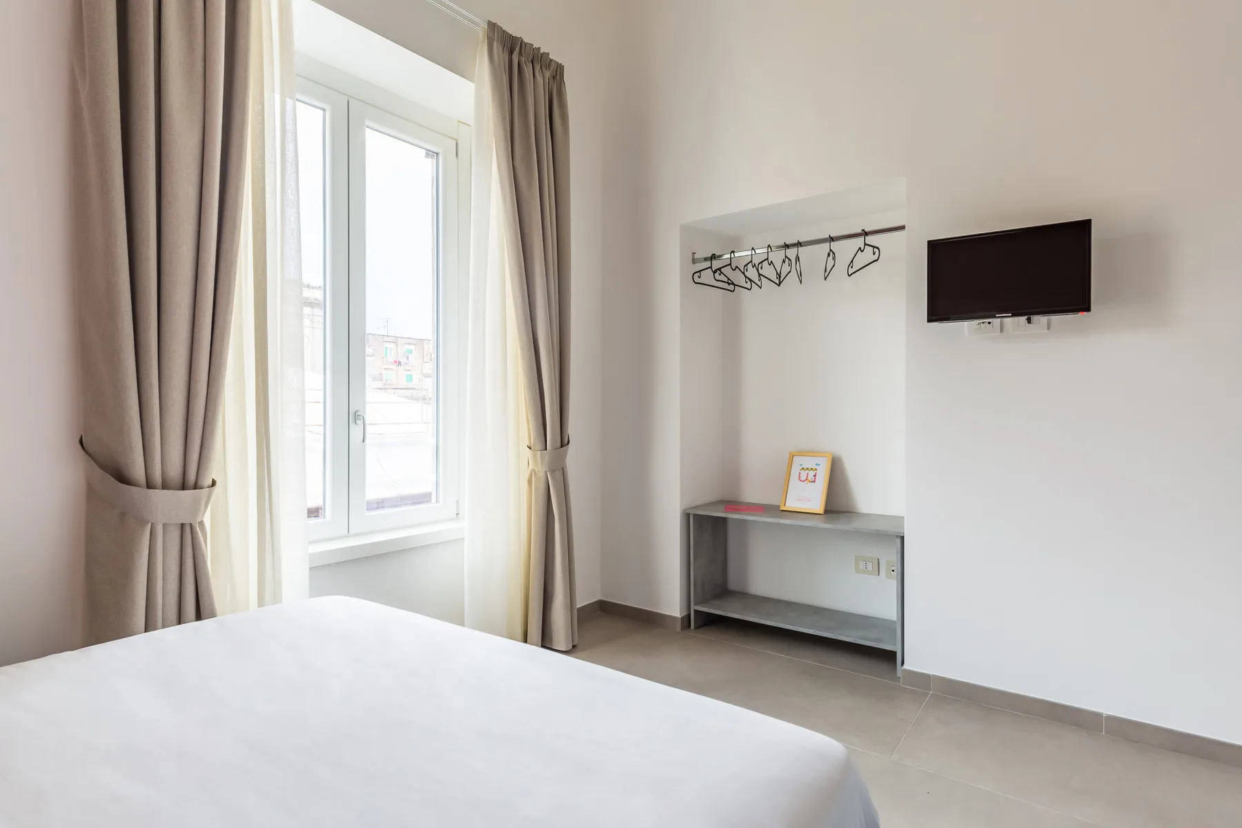 Un dormitorio con una cama, una ventana con cortinas y un televisor en la pared.