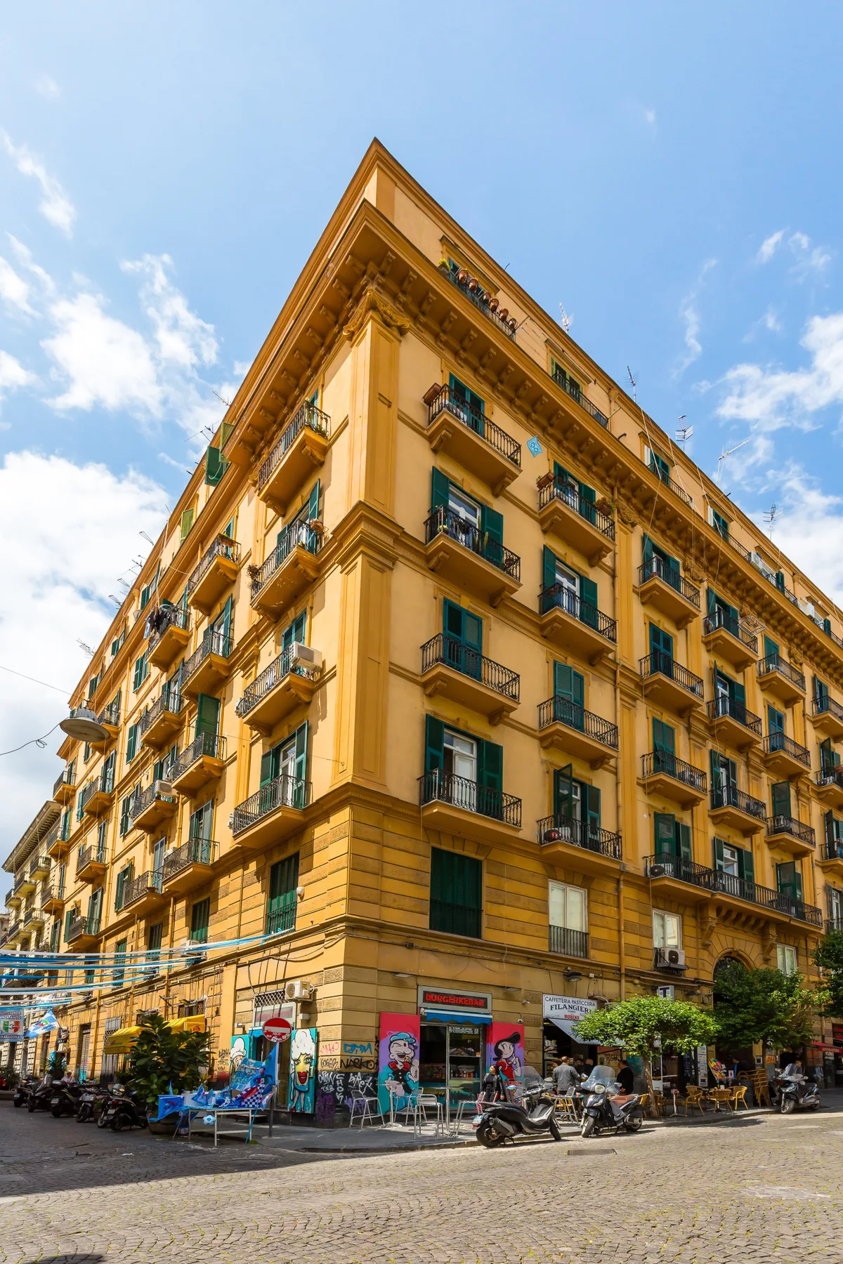 Un edificio amarillo de varios pisos con balcones se alza en una calle urbana.