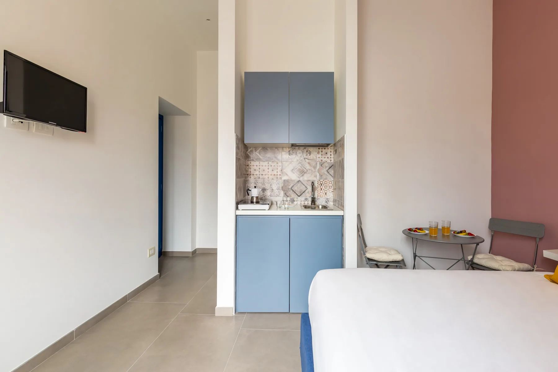Una habitación con cama, televisor montado en la pared y una pequeña cocina.