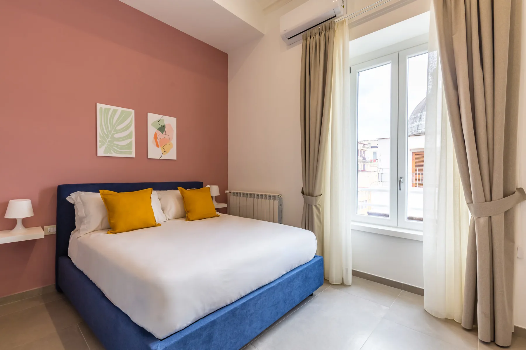 Un dormitorio con una cama y ventanas altas enmarcadas por cortinas.