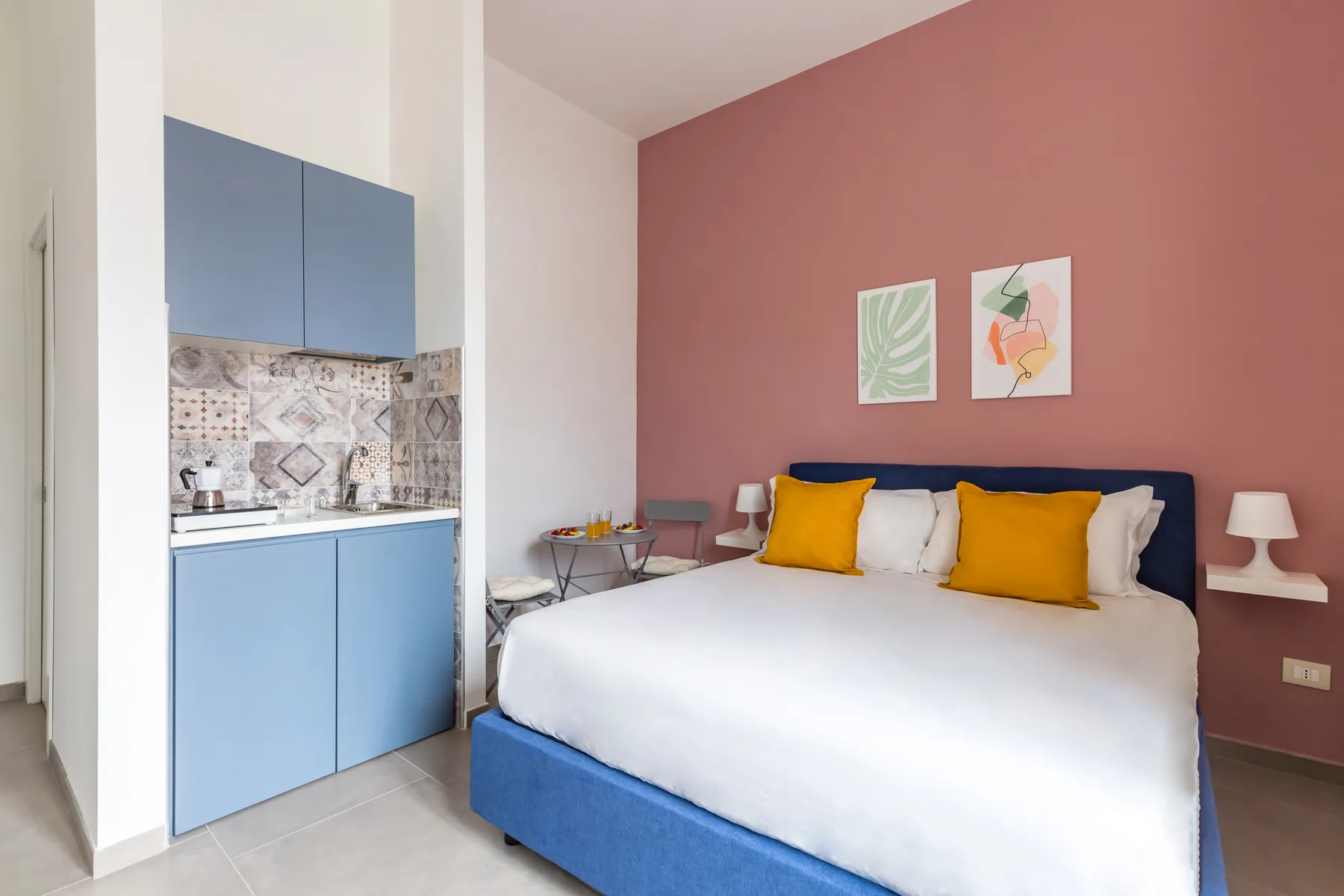 Un dormitorio con una cama grande, gabinetes azules de cocina y una pared rosa.