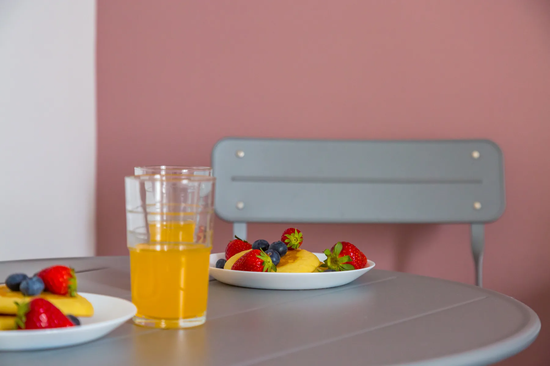 Una mesa de comedor con platos de fruta y un vaso de zumo de naranja.