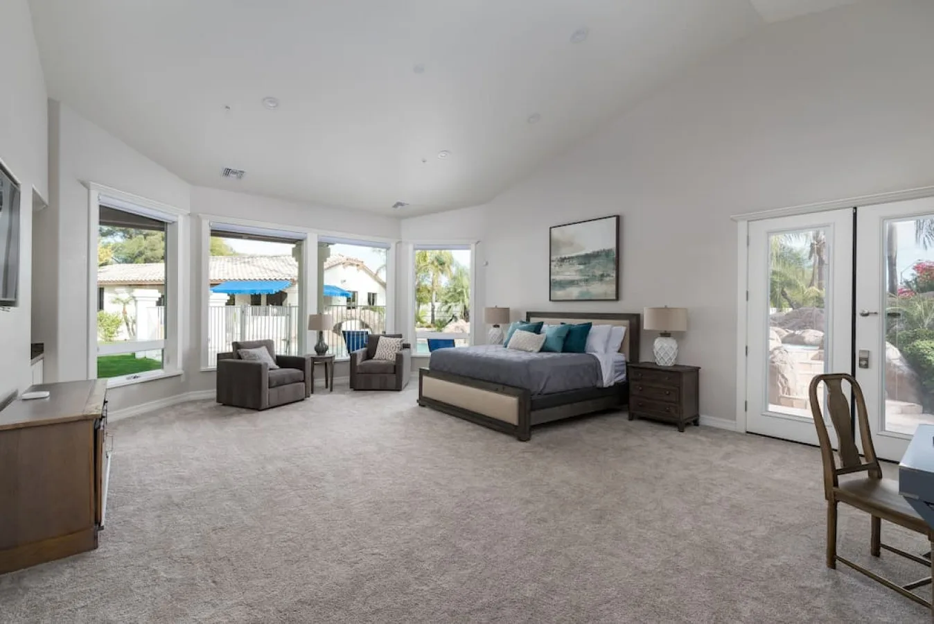 A spacious bedroom with a bed, seating area, and large windows.