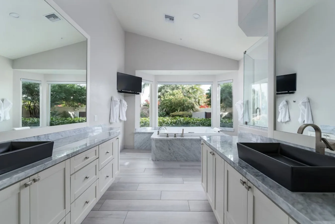 A bright bathroom with long vanities and a large tub beneath the windows.