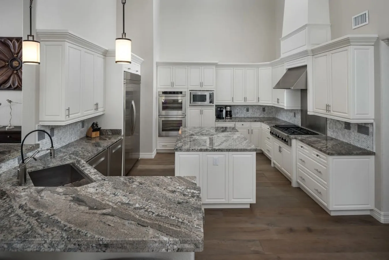 A spacious kitchen with white cabinetry, stone countertops, and stainless steel appliances.