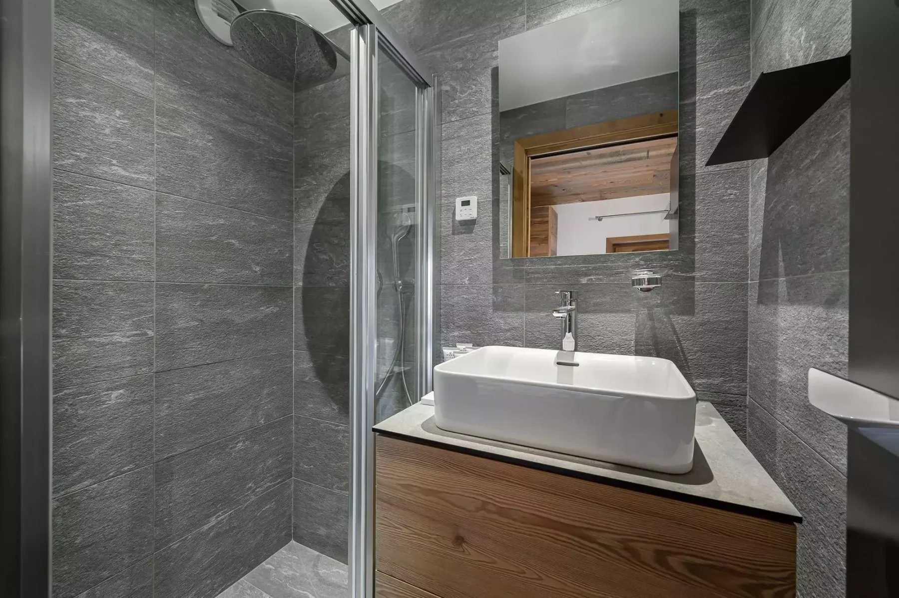 Baño moderno con lavabo sobre mueble y ducha de vidrio.