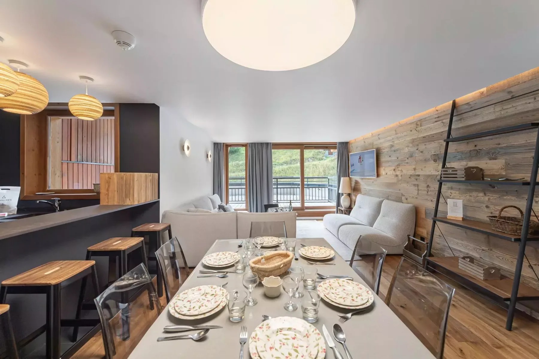 A dining table and seating occupy a bright living area beside a kitchen counter.