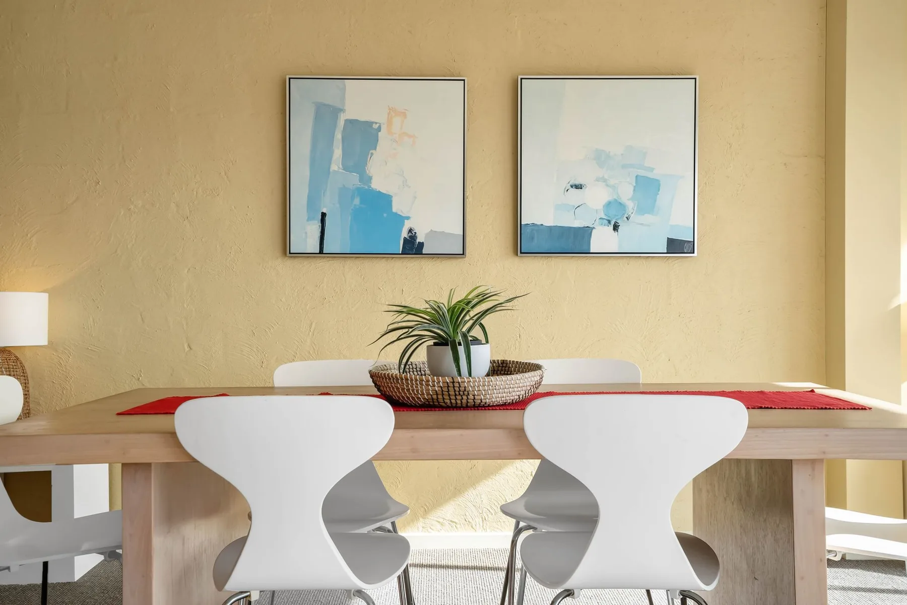 A dining area with a wooden table, white seating, and framed artwork.