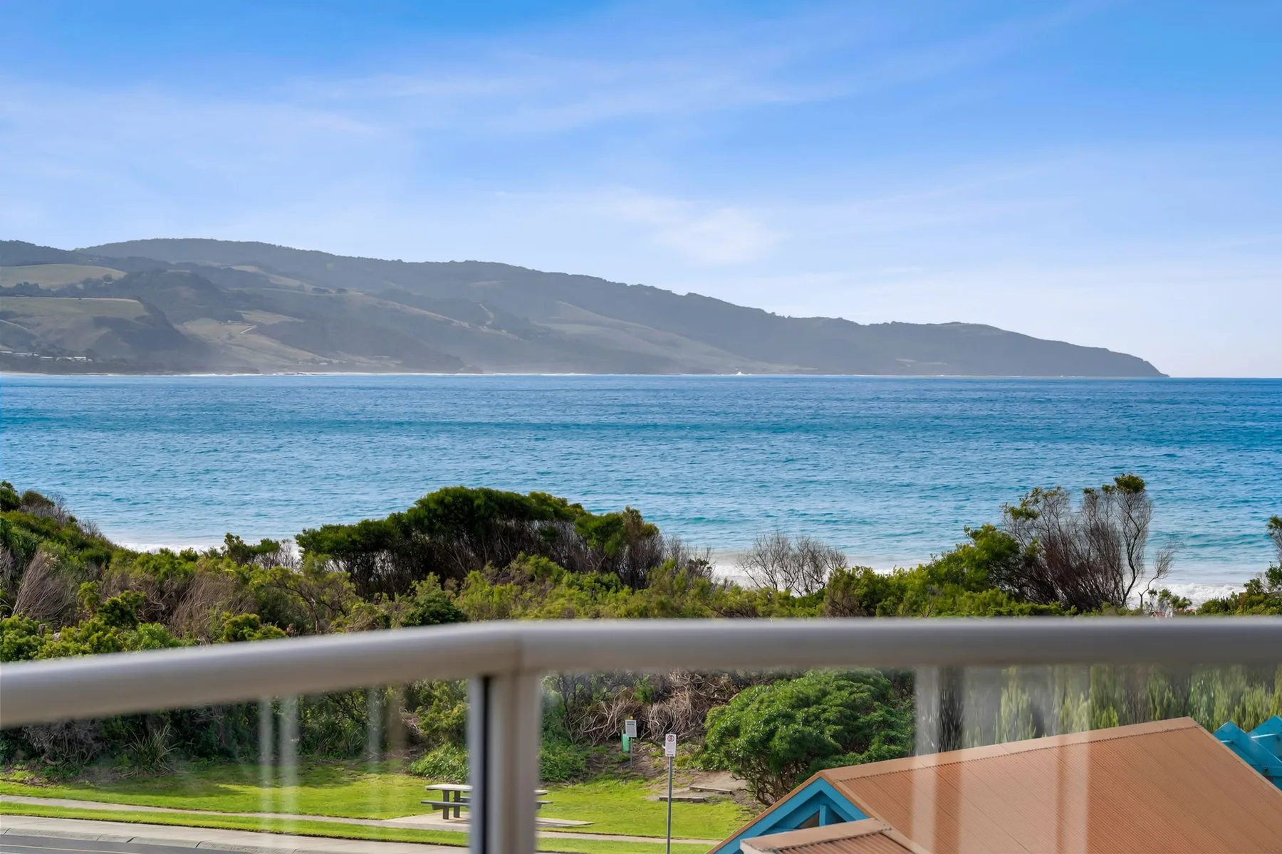Coastal view from a balcony overlooking the sea and distant hills.
