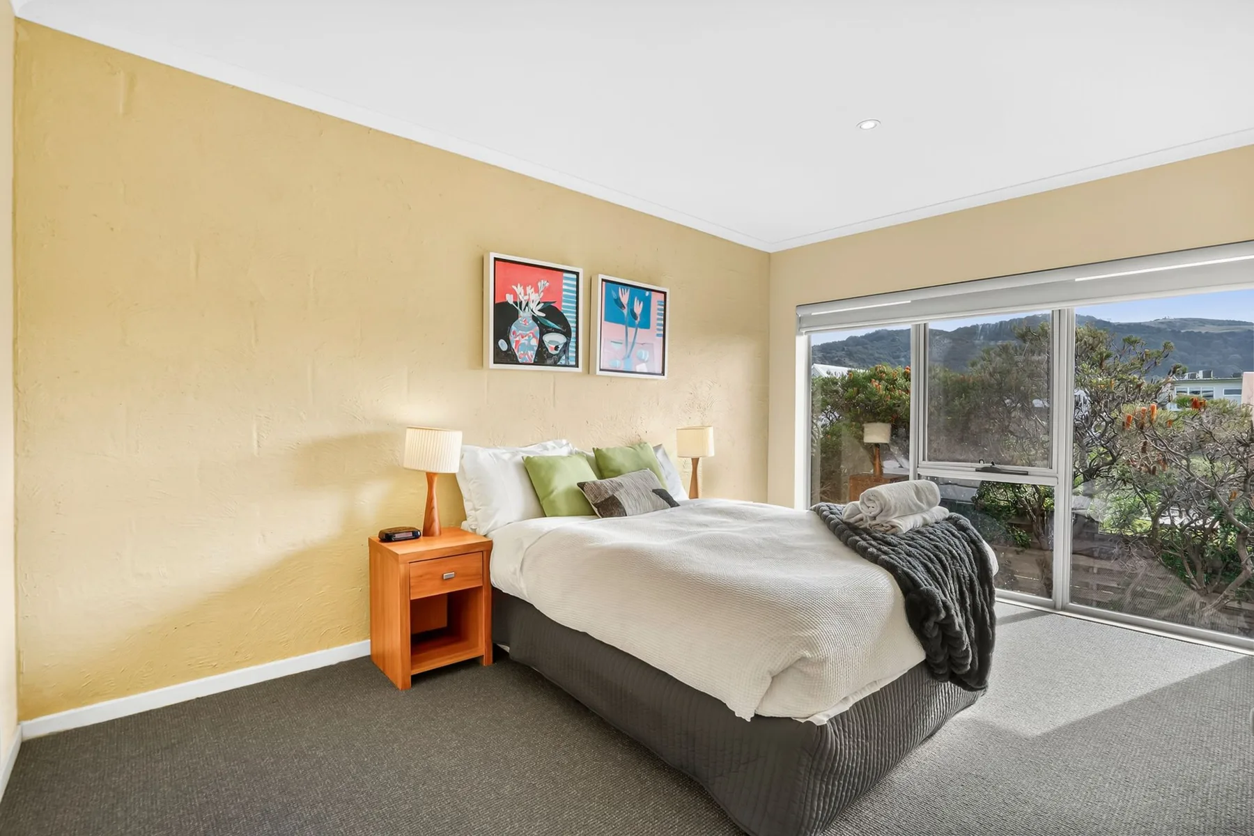 A bedroom with a bed beside a large window overlooking greenery.