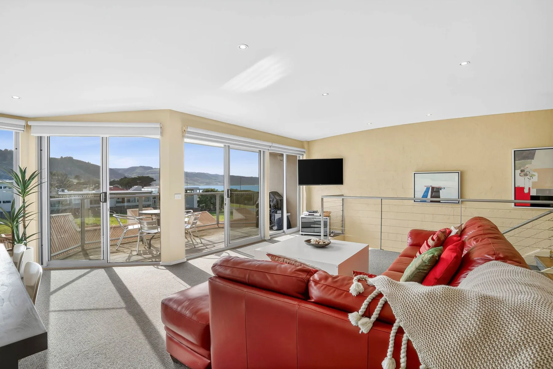 A bright living room with red seating and large windows overlooking the water.