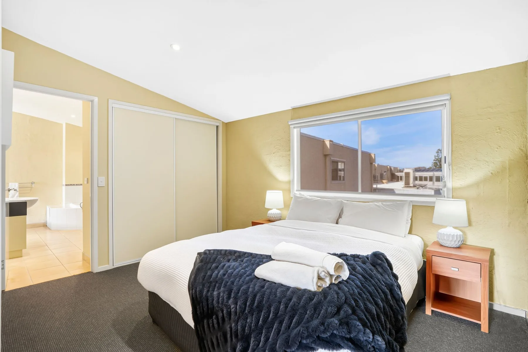 A bright bedroom with a neatly made bed and a large window.