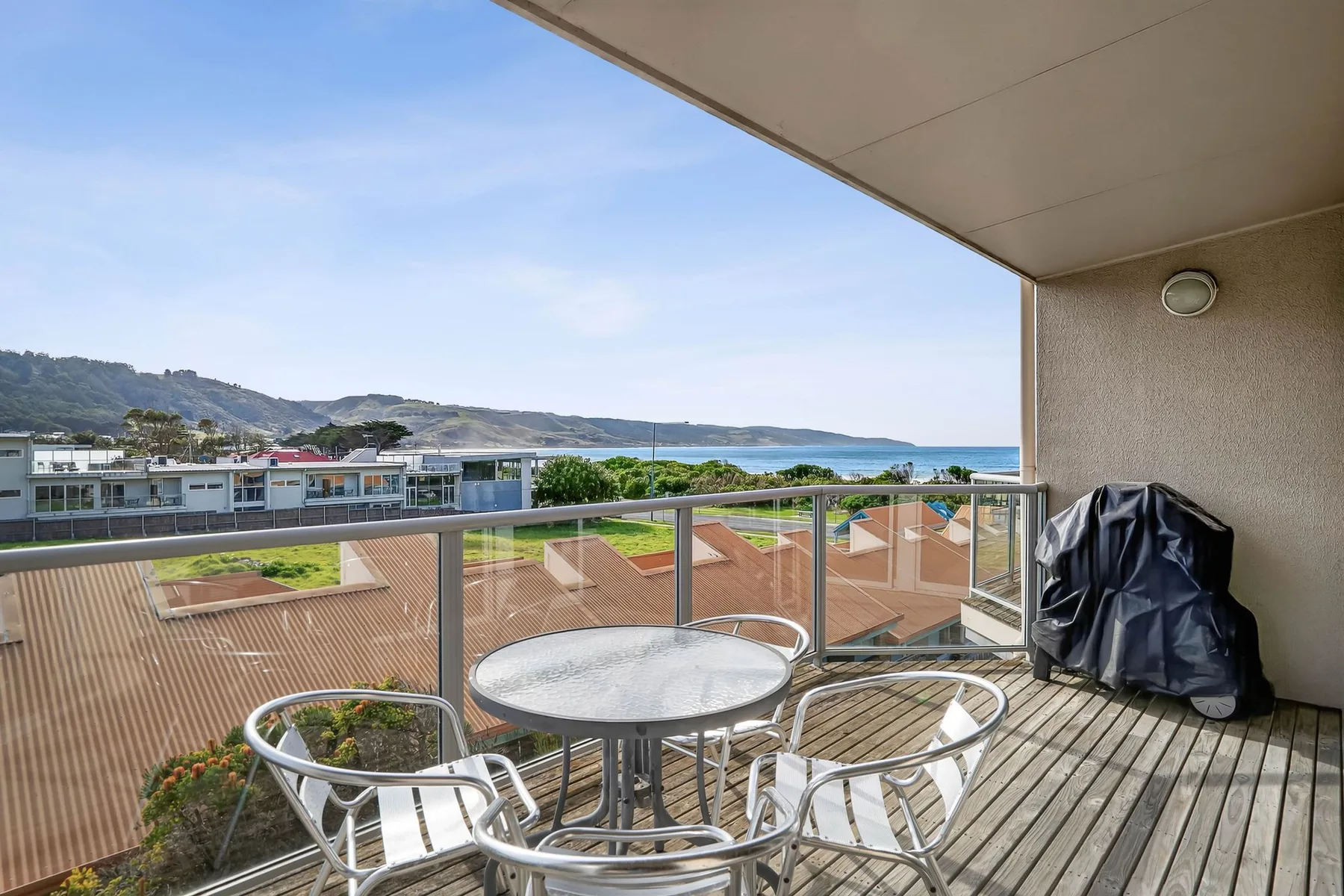 A balcony seating area overlooks nearby rooftops, hills, and the water.