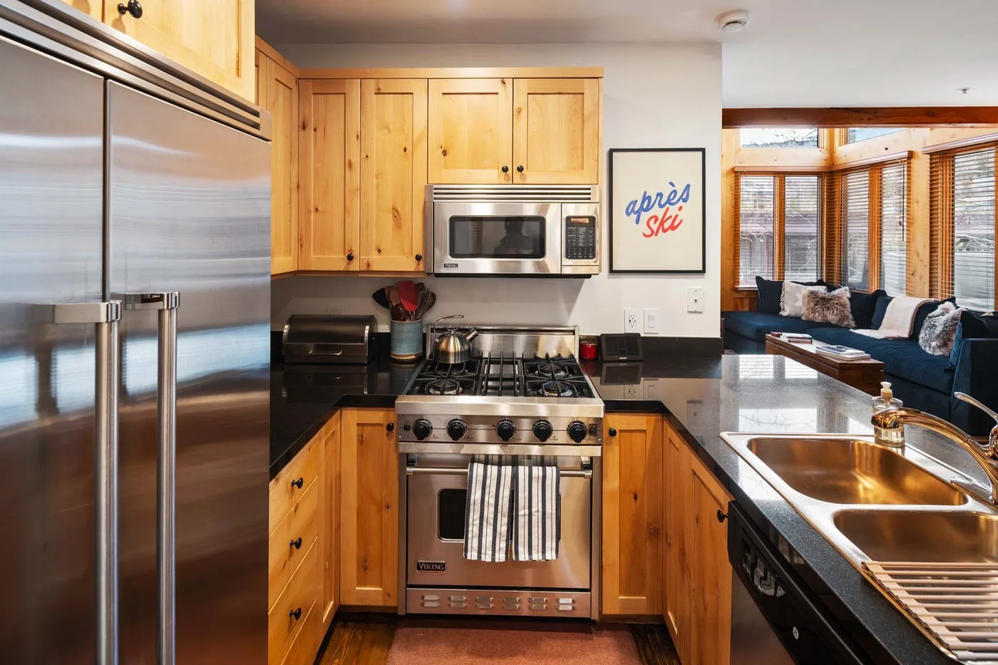 Una cocina con gabinetes de madera y electrodomésticos de acero inoxidable da a una zona de estar.