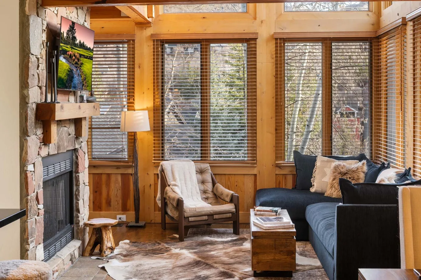 Una sala de estar revestida de madera con chimenea, asientos y grandes ventanas.