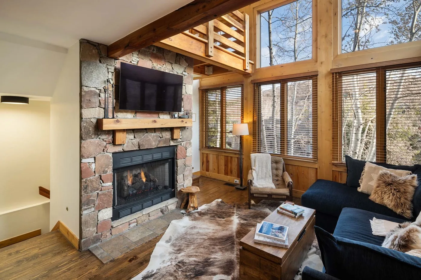 A wood-paneled living room with a stone fireplace, large windows, and seating.