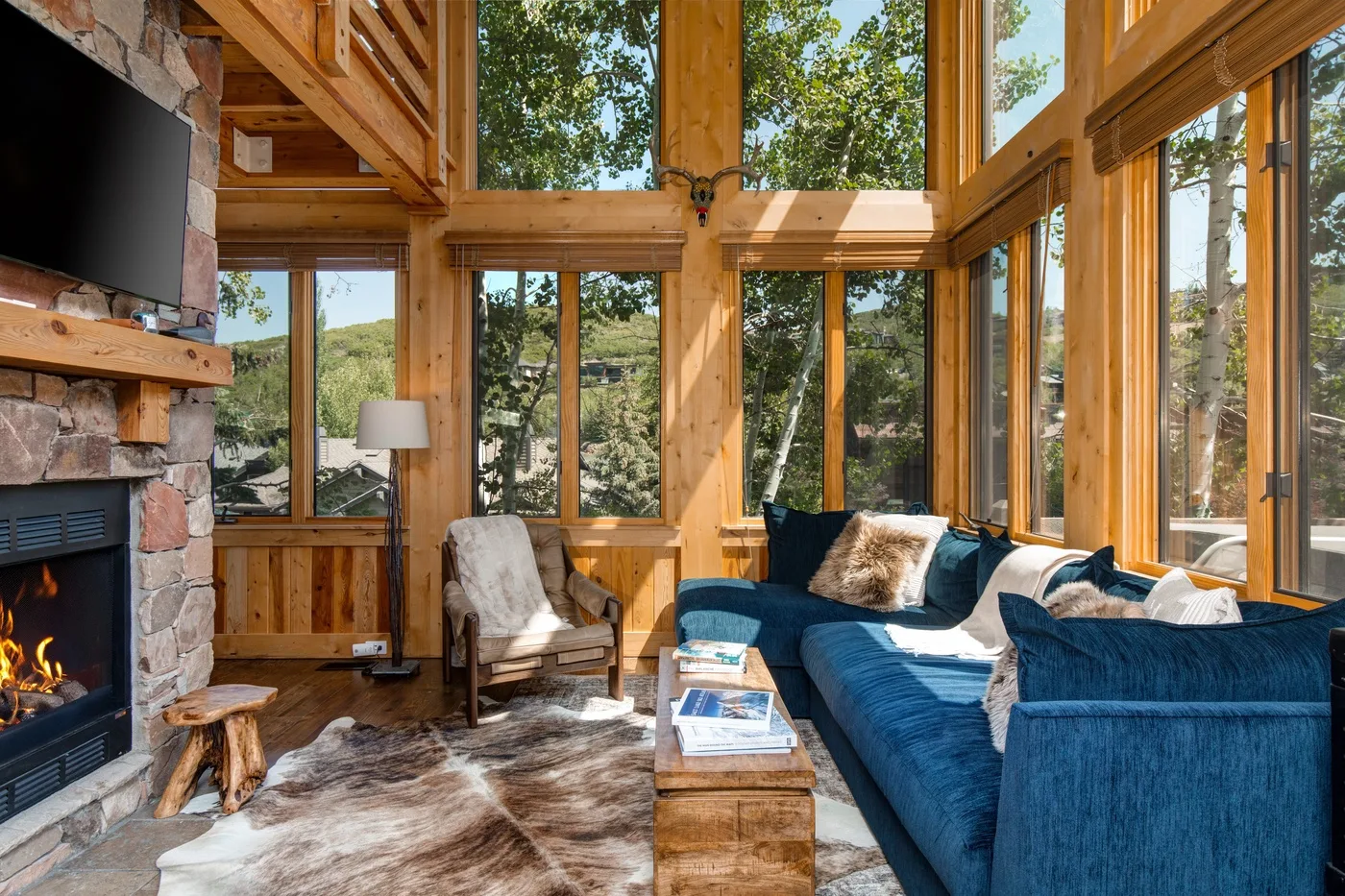 Una sala de estar luminosa con grandes ventanas, asientos azules y una chimenea de piedra.