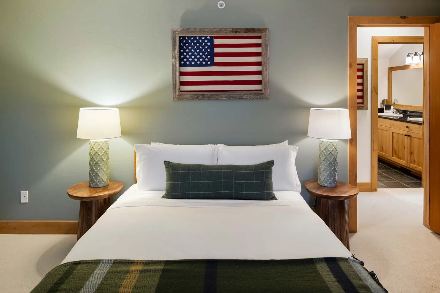 Un dormitorio con una cama bien hecha, lámparas de noche a juego y una bandera enmarcada.