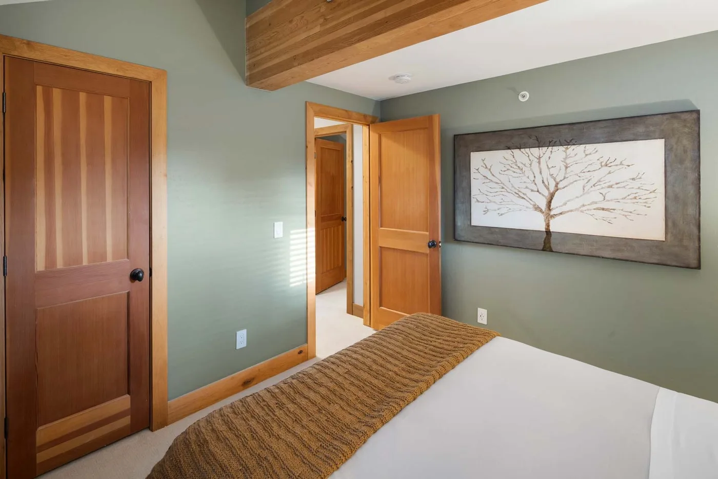 Un dormitorio con una cama, puertas de madera y un cuadro de un árbol en la pared.