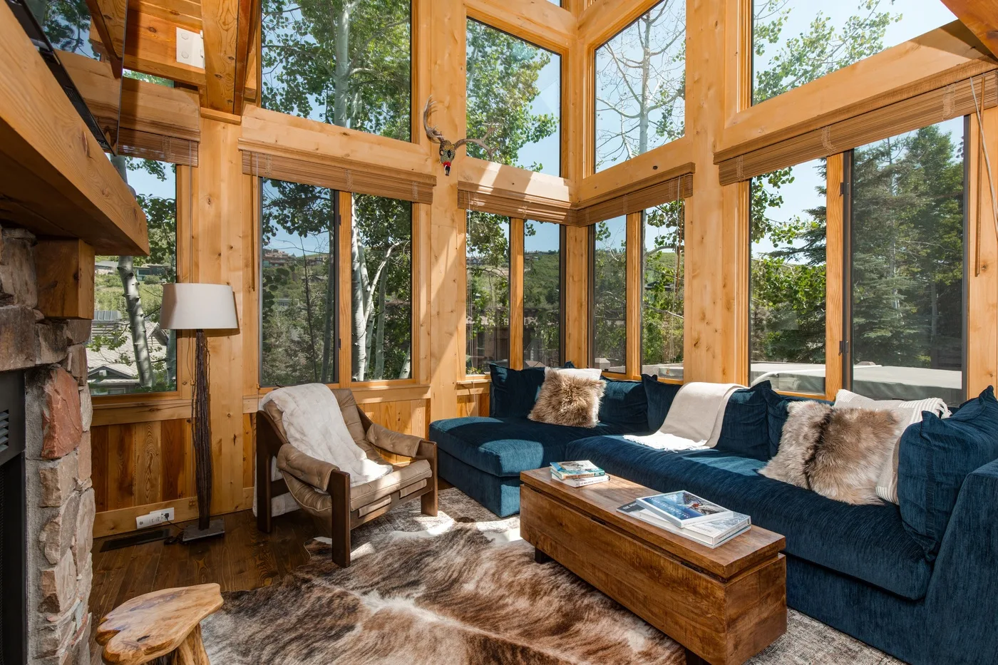A bright living room with tall windows, blue seating, and a wooden coffee table.