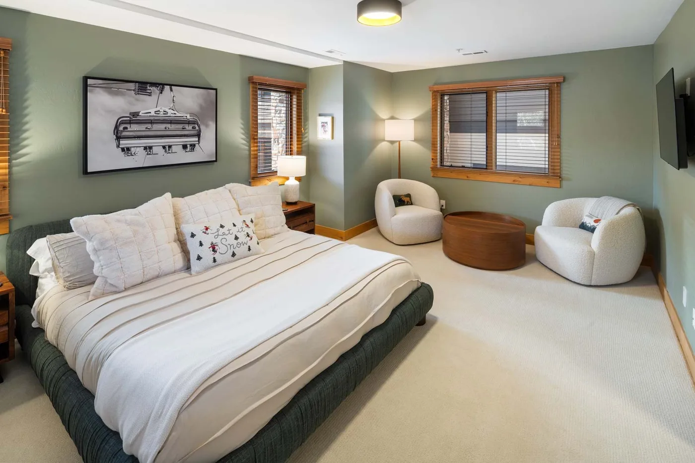 Un dormitorio con una cama grande, dos sillones redondeados y ventanas con persianas de madera.