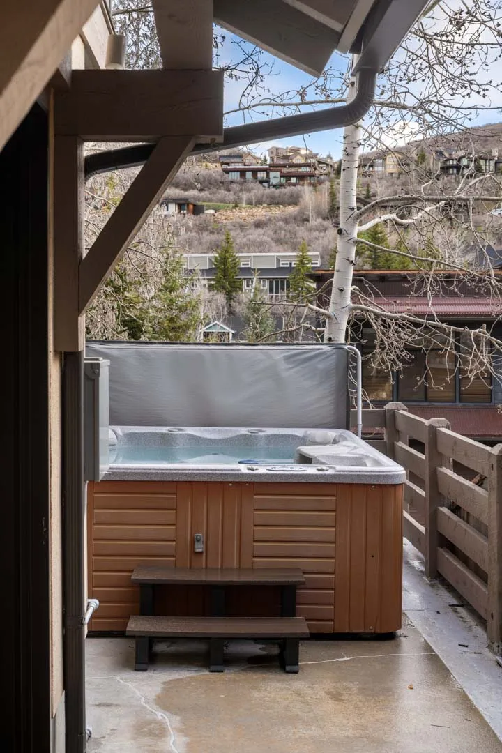 Una bañera de hidromasaje al aire libre está en un patio cubierto junto a una barandilla de madera.