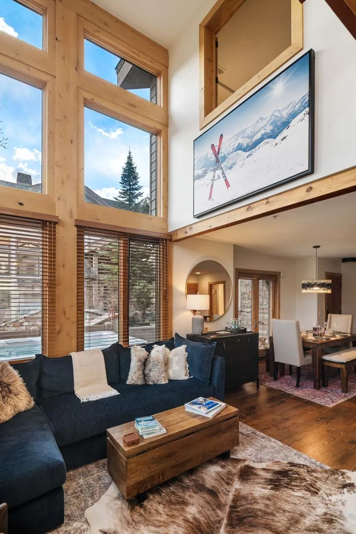 Una sala y comedor de doble altura con grandes ventanas y una zona de asientos oscura.