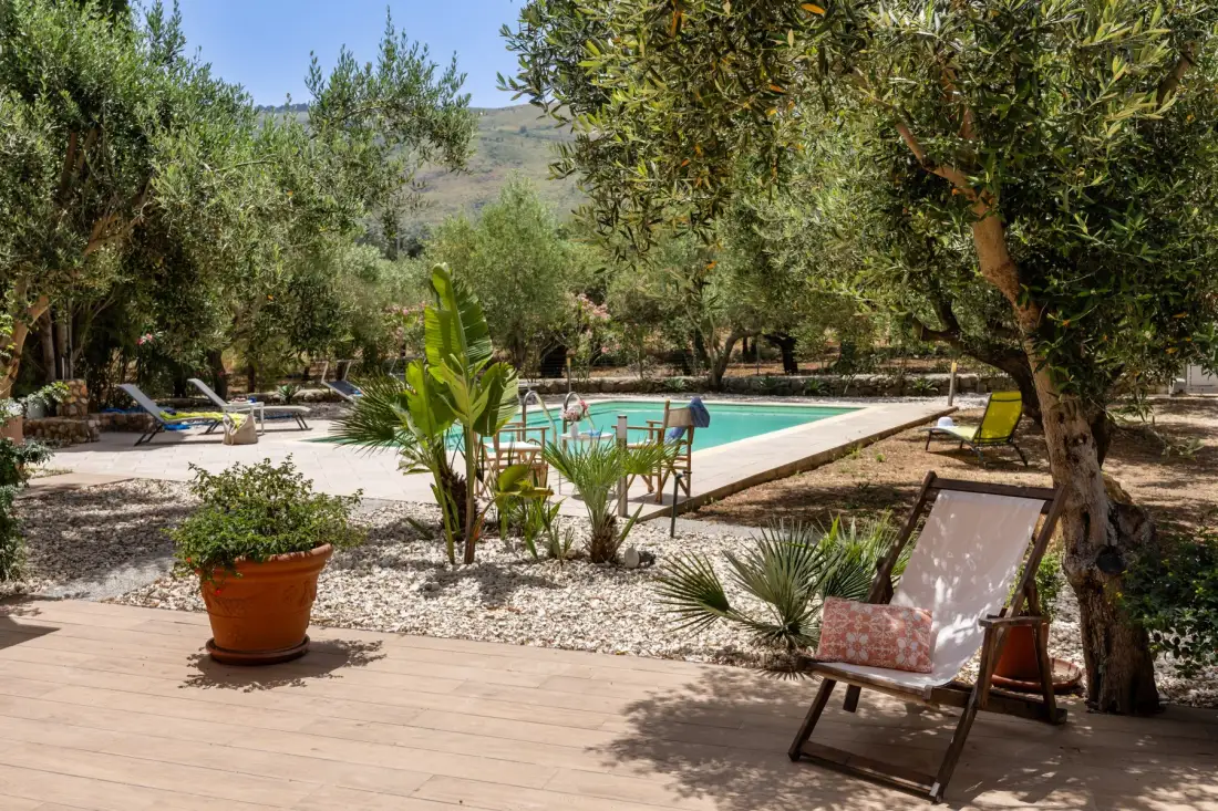 A garden patio overlooks a swimming pool, with loungers among the trees.
