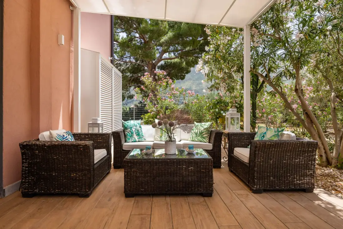 A covered outdoor seating area with a low table and leafy trees beyond.