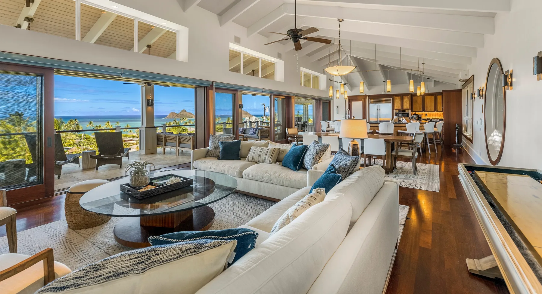 Una sala de estar y comedor abiertos, con asientos junto a grandes ventanas con vista al agua.