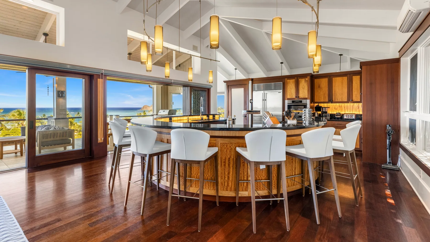 Una cocina luminosa con una isla curva y asientos de barra junto a grandes ventanales.