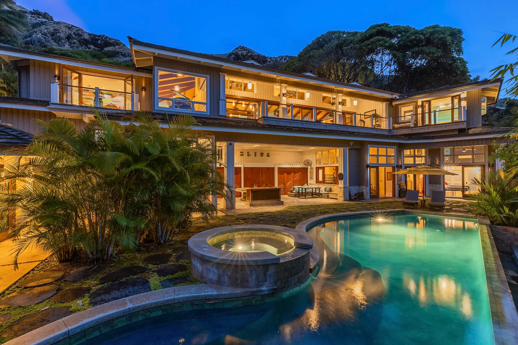 Una casa moderna grande da a una piscina iluminada y un spa circular al anochecer.