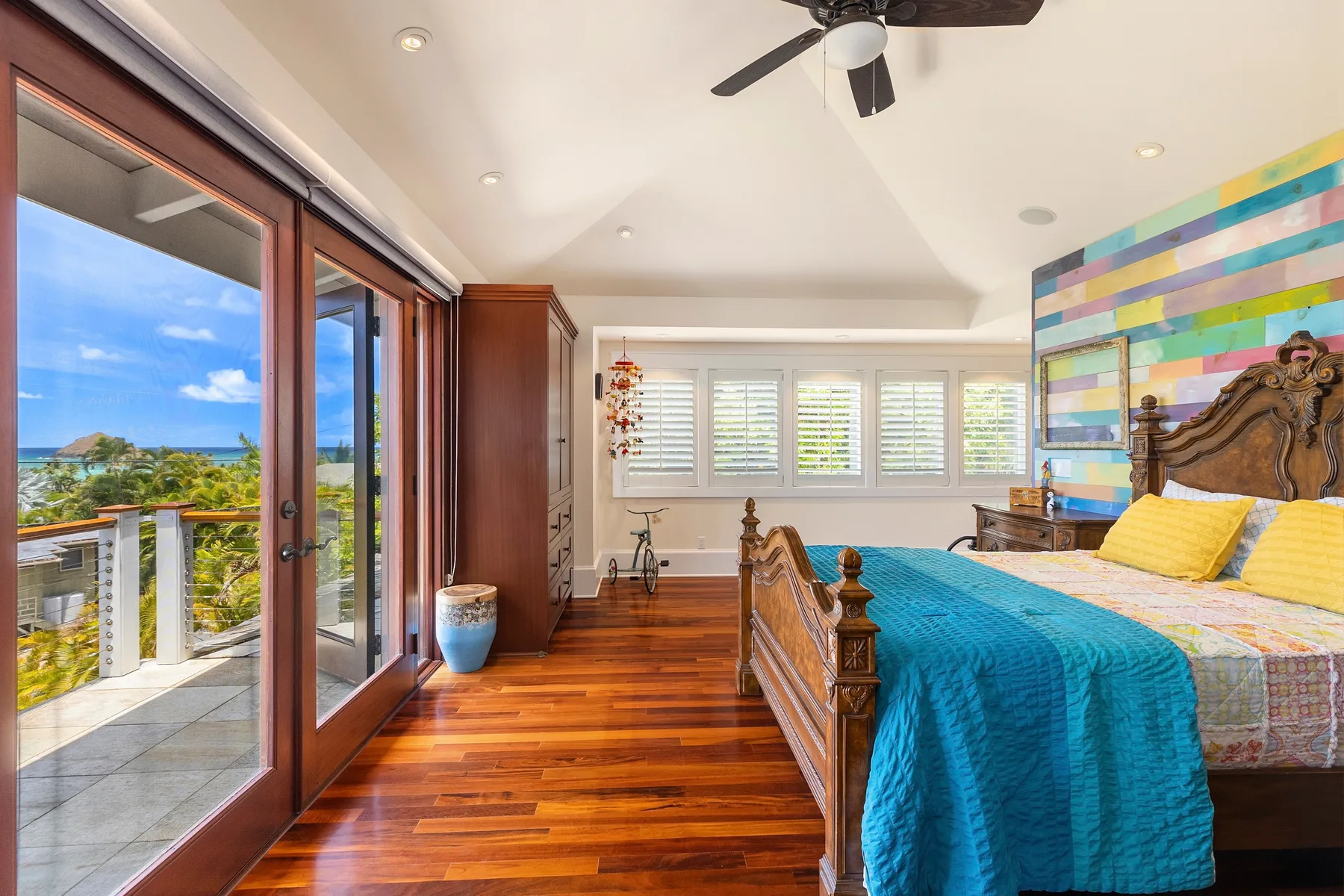Un dormitorio con una cama de madera, ropa de cama azul y ventanas con vistas al agua.