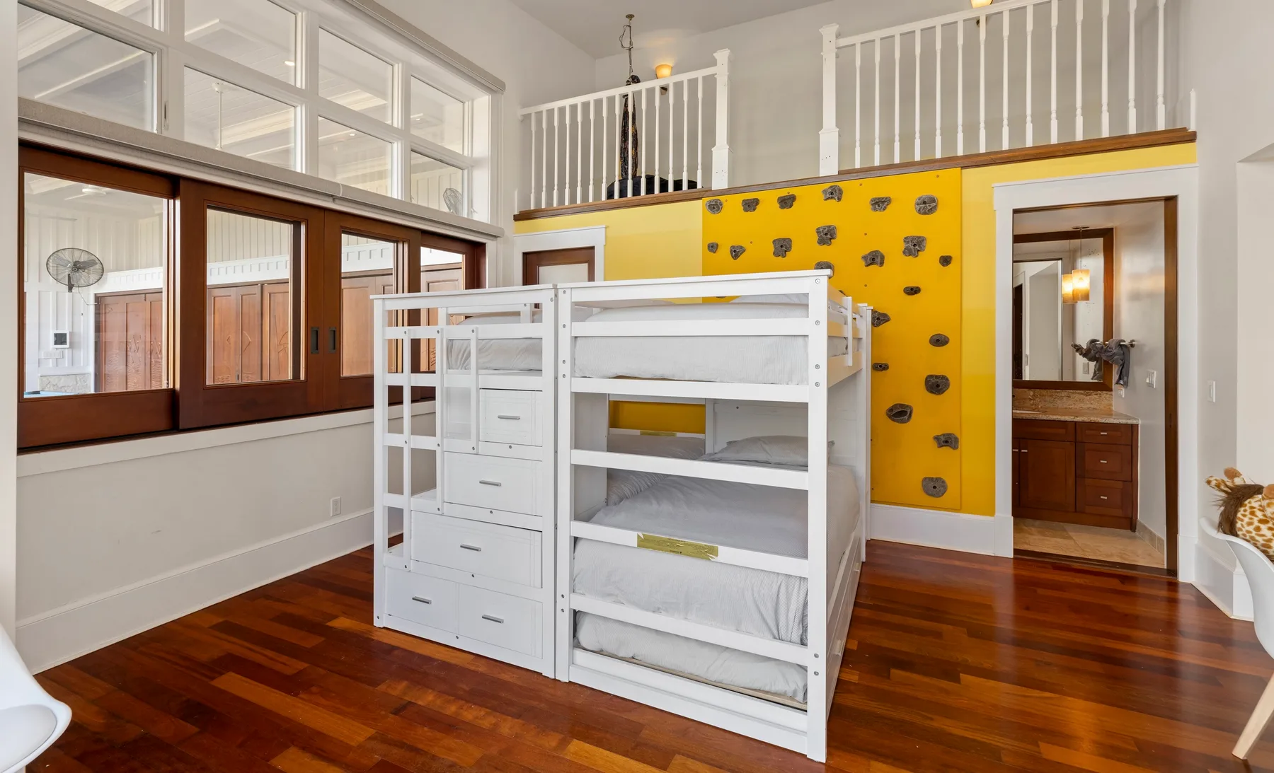 Un dormitorio luminoso con literas blancas y un muro de escalada amarillo.