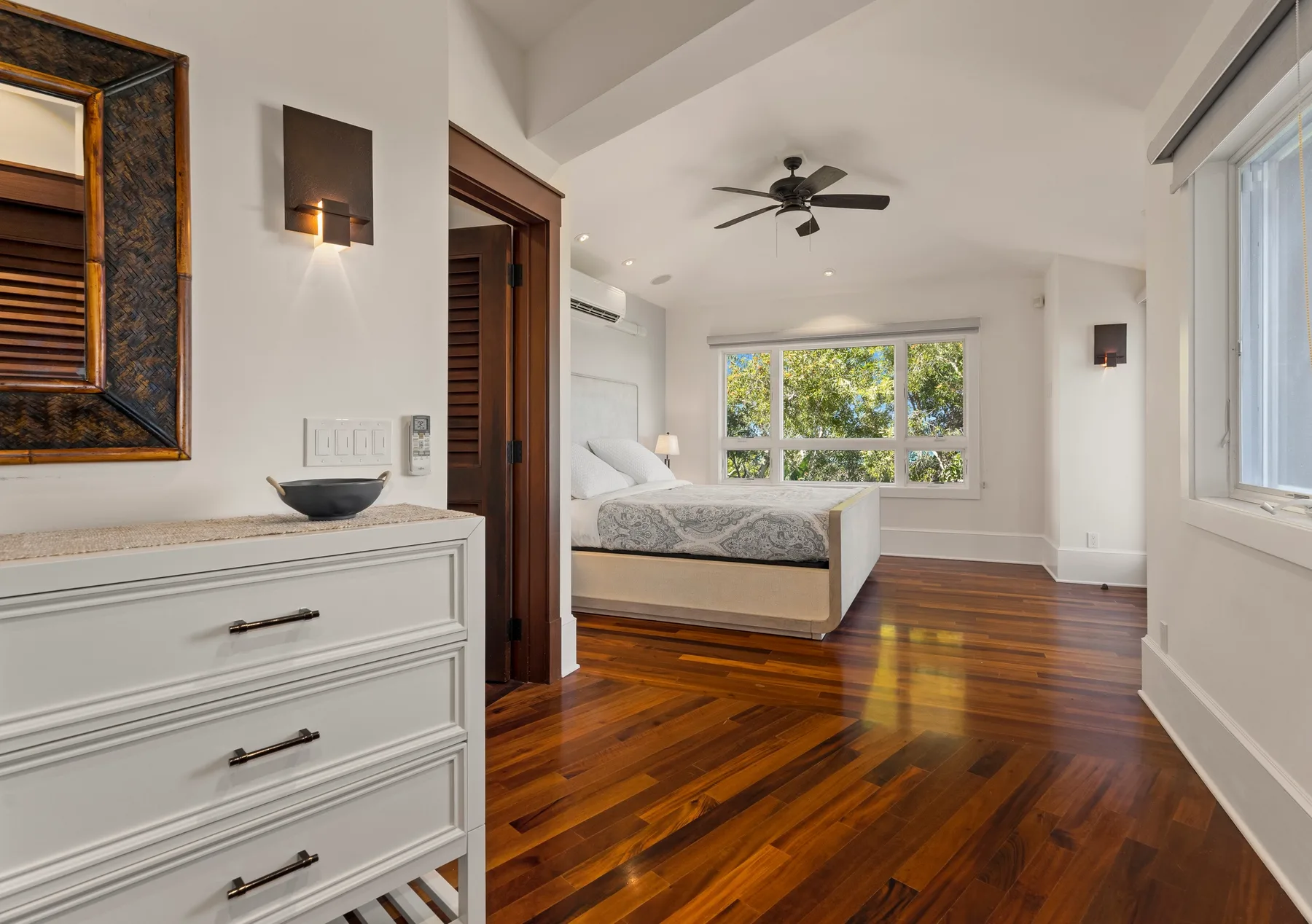 Un dormitorio luminoso con una cama, suelo de madera y ventanas grandes.