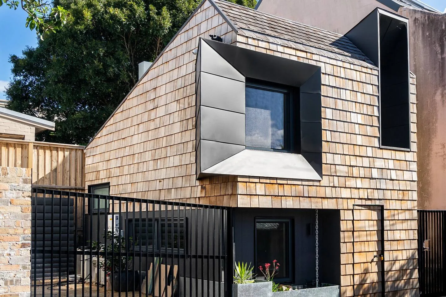 El exterior de una casa moderna tiene revestimiento de aspecto escamoso y ventanas con marcos oscuros.