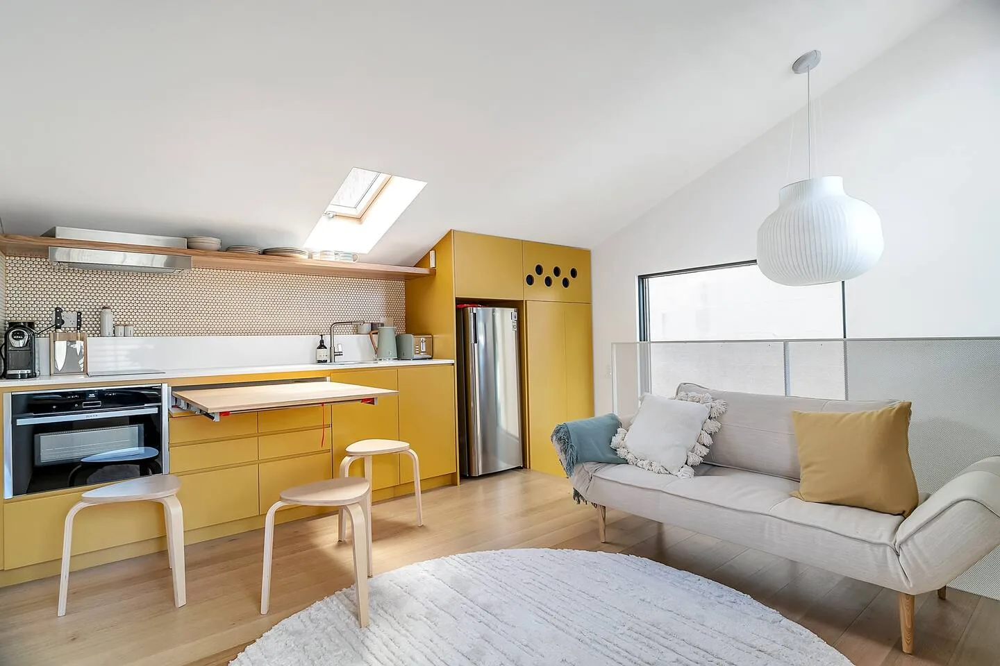 A bright open-plan kitchen and living area has a sofa beside a dining table.