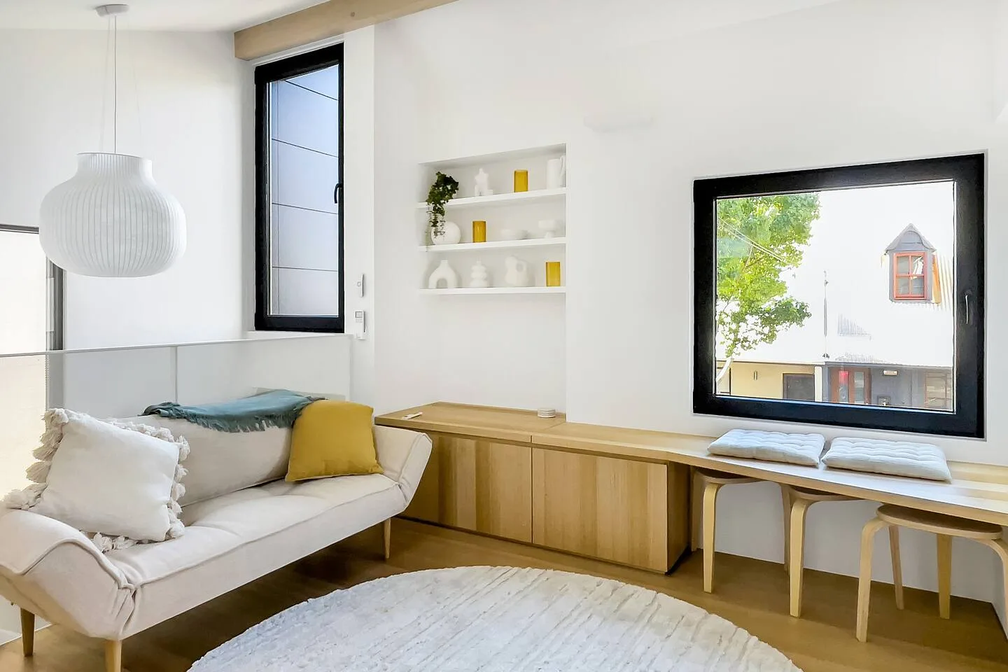 Una sala luminosa con asientos junto a un mueble largo de madera y ventanas amplias.