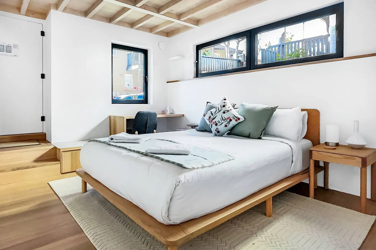 Un dormitorio con una cama bien arreglada, cojines decorativos y ventanas en la pared.