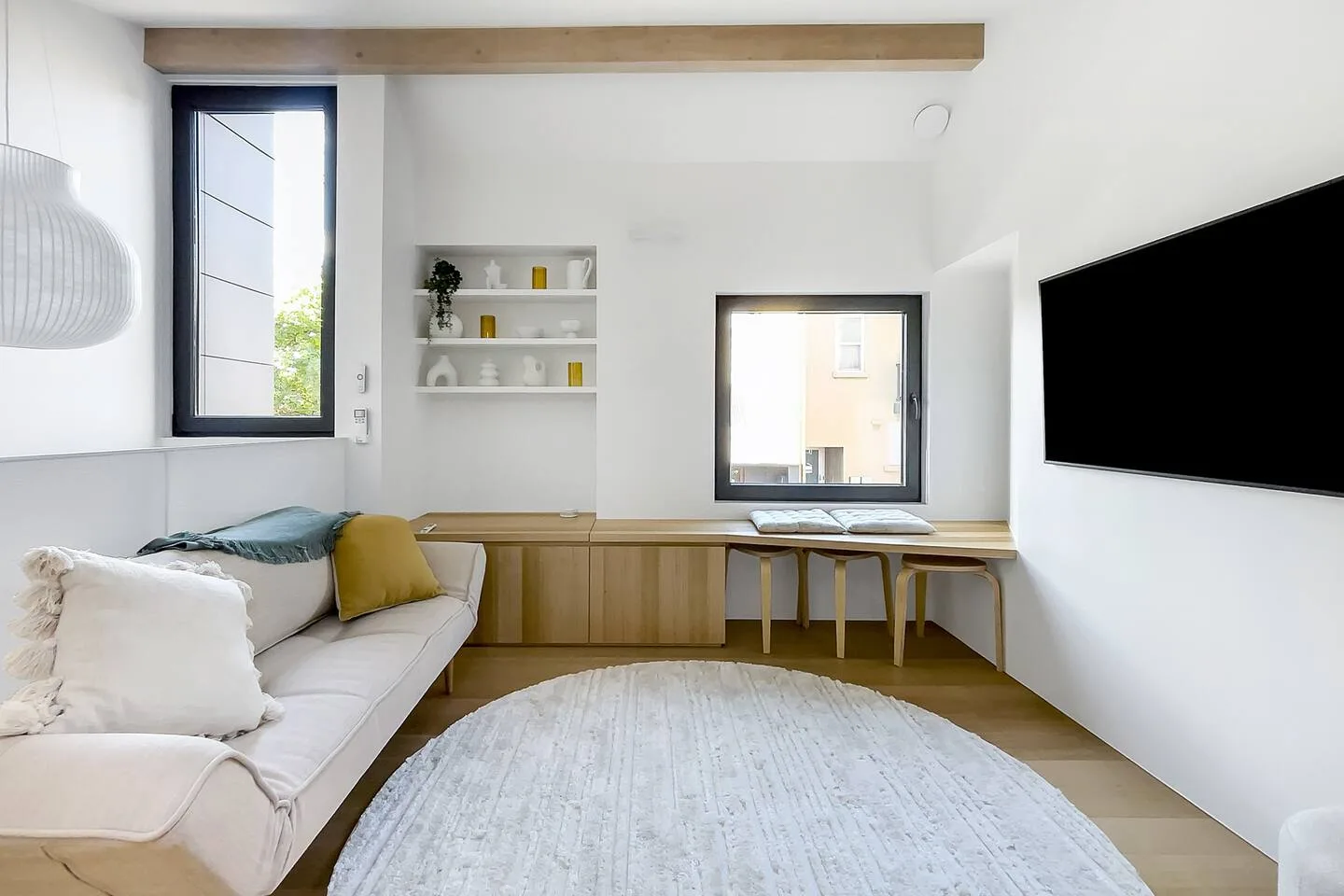 A bright living area with seating, a wall-mounted television, and a desk by the window.