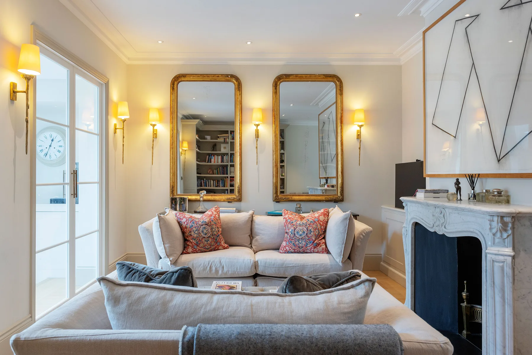A bright living room with seating, framed mirrors, and a fireplace.