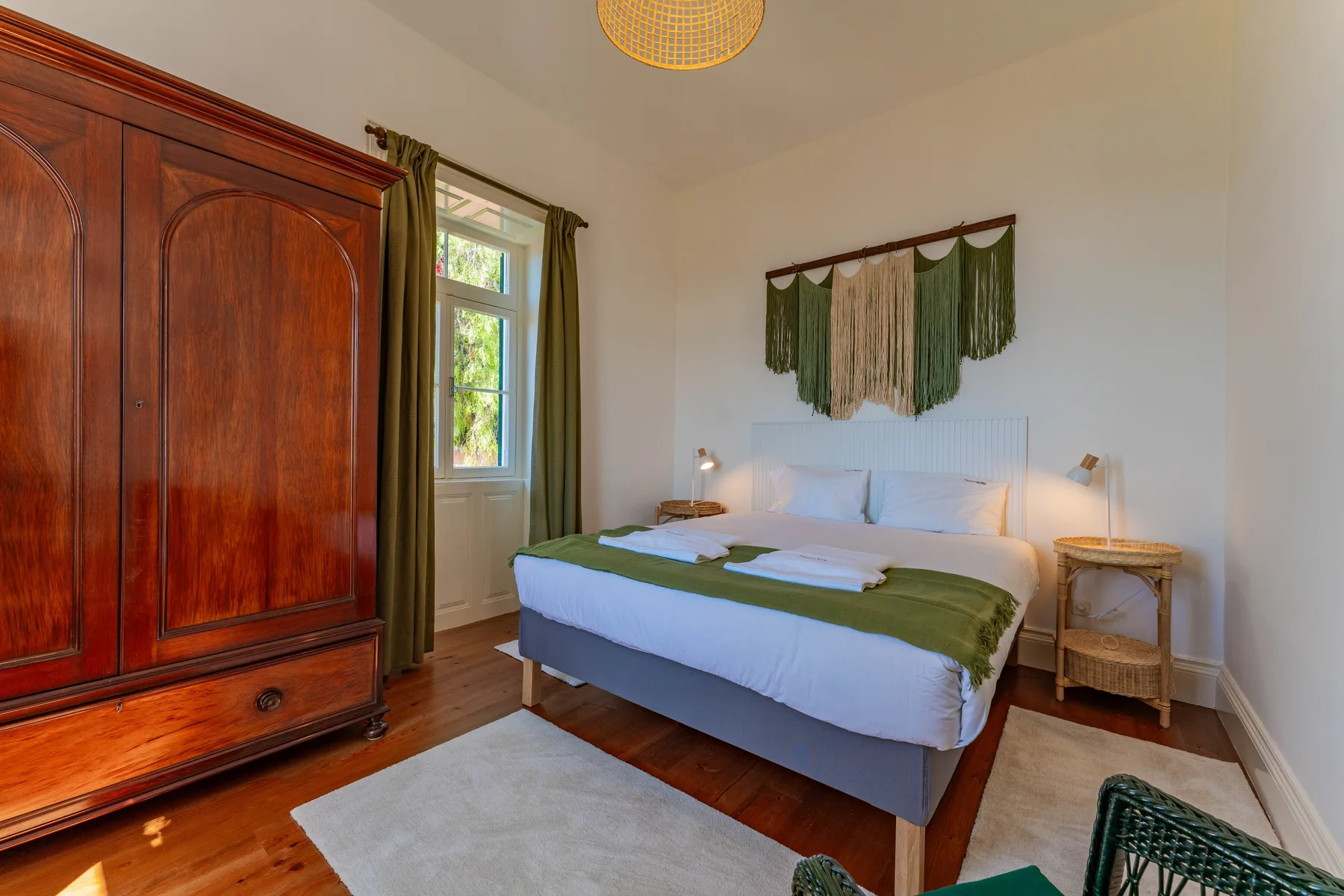 Un dormitorio con una cama vestida de blanco y verde junto a un armario de madera.