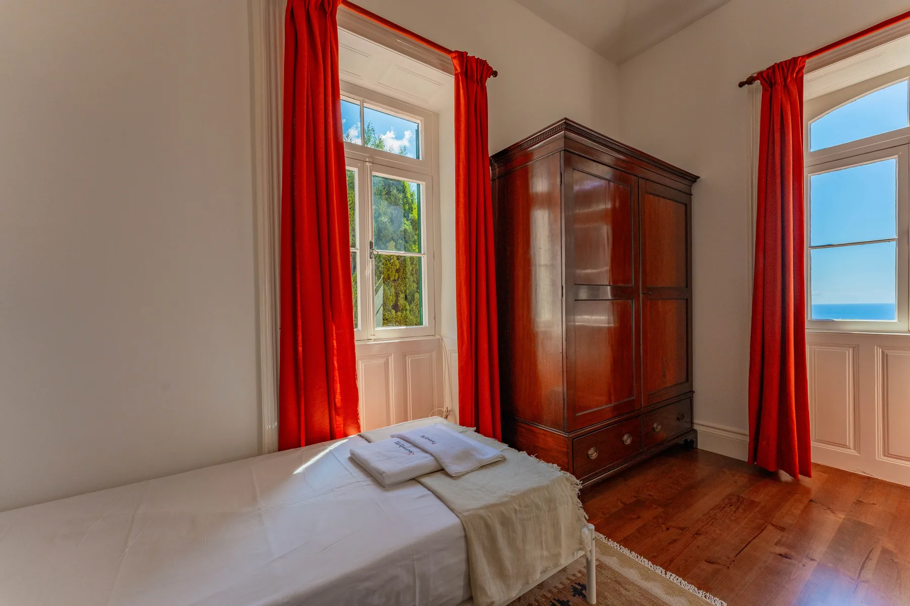 Un dormitorio con una cama, un armario de madera y cortinas rojas.