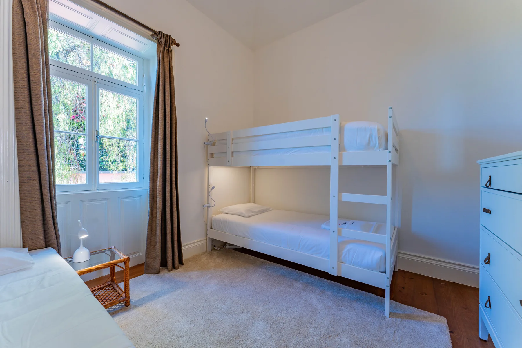 Un dormitorio con literas blancas junto a una ventana alta.