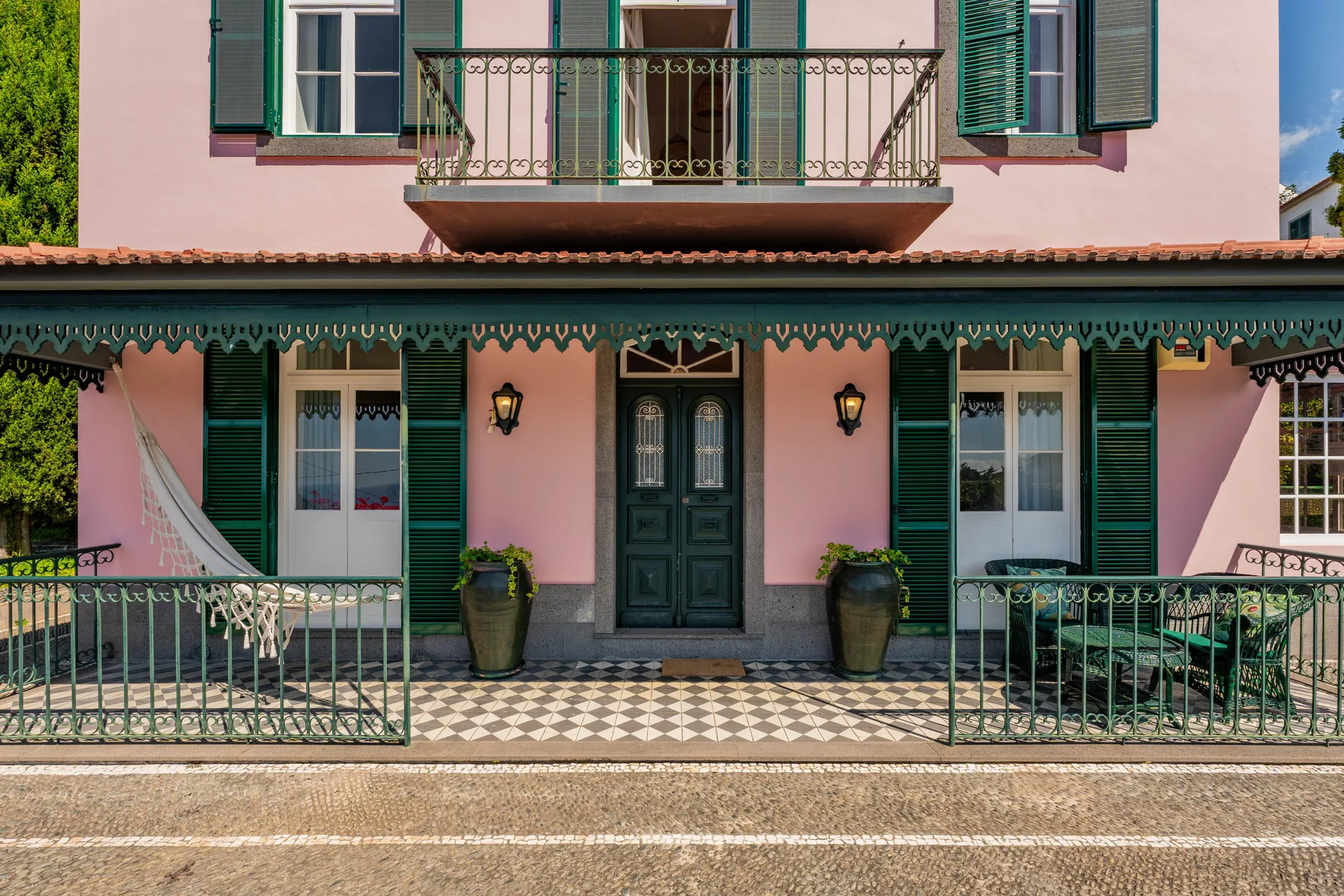 Fachada de una casa rosa con contraventanas verdes y una puerta principal oscura.