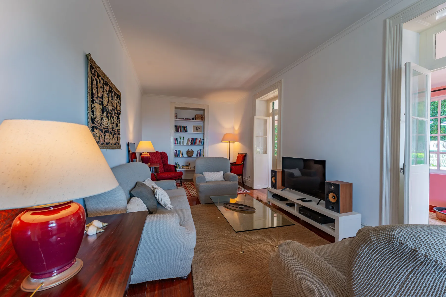 Una sala de estar con asientos, un televisor y puertas abiertas a un balcón.