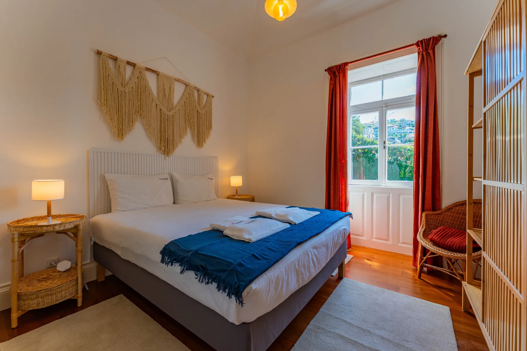 Un dormitorio con una cama vestida con ropa de cama blanca y azul junto a una ventana luminosa.