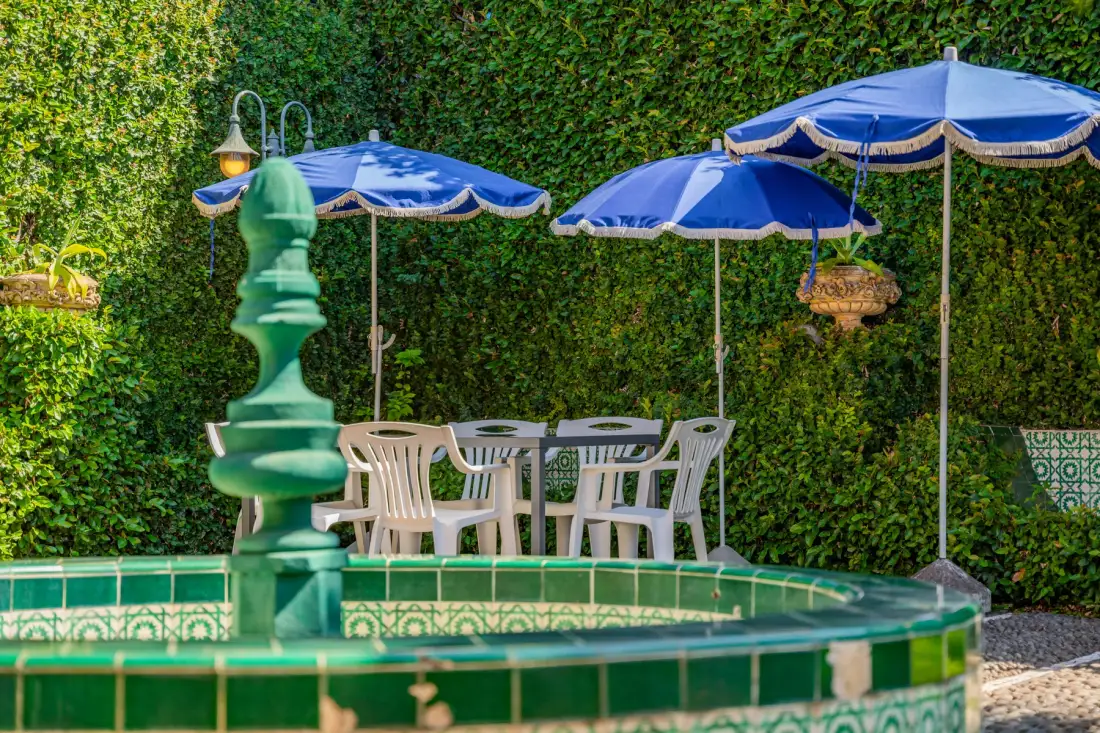 Un patio al aire libre con una fuente de azulejos, asientos de comedor y sombrillas azules.
